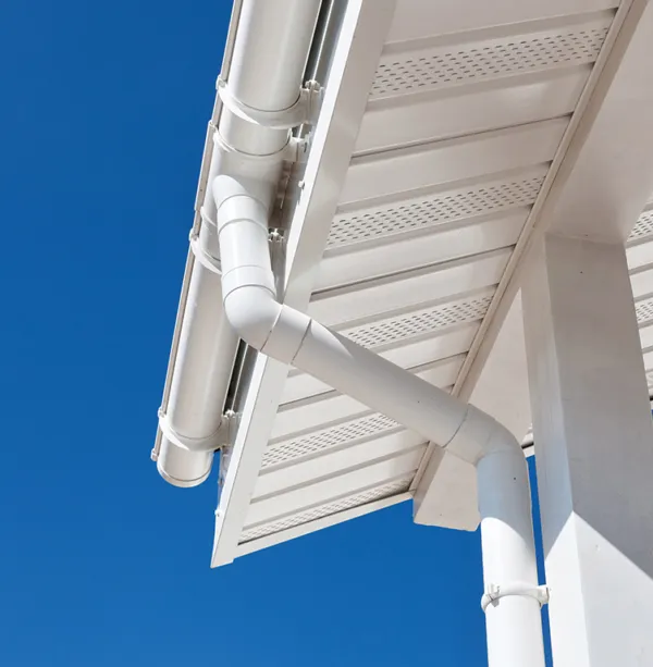 Close-up of a white seamless gutter and downpipe corner joint installed under the roof fascia